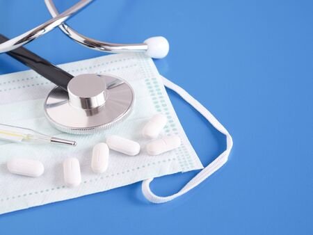 A pill, Thermometer, stethoscope and protective face mask on the blue background. Health concept. Copy space.の写真素材
