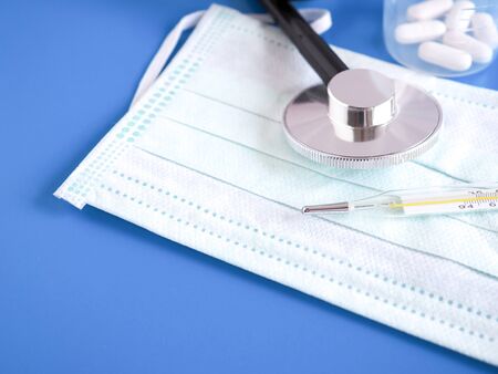 Thermometer, stethoscope and protective face mask on the blue background. Health concept. Copy space.の写真素材