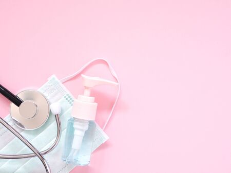 The alcohol gel in the bottle pump with a protective face mask and  stethoscope on a pink background. Health concept with copy space. Top view, Flat lay.の写真素材