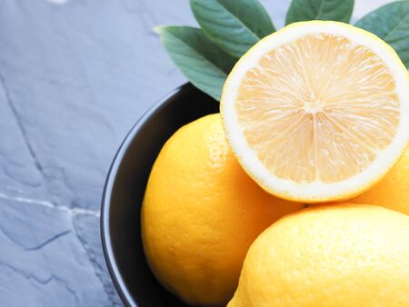 Half and group of fresh lemon with leaves in black bowl on black stone background.  Copy space for text. High Vitamin C.の写真素材