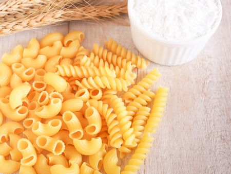 Variety of shaped Italian pasta and flour in a small bowl on white wooden table background.の写真素材