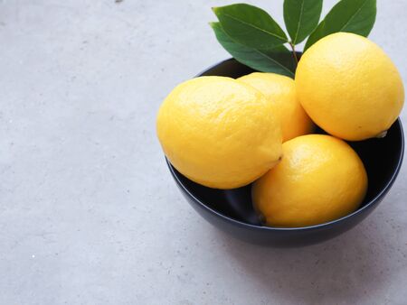 Close up lemon fruit with leaves in black bowl on grey background. Copy space.の写真素材