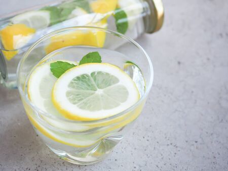 Water and lemons slice in glass with mint leaves and bottle on grey background, drink for detox, and refresh the body.の写真素材