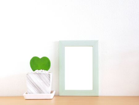 Green border photo frame and heart-shaped tree in a flower pot placed on a wooden shelf with a white wall as the background.の写真素材