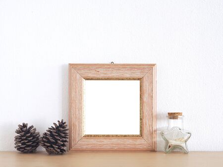 Wood picture frame and pine cones, star-shaped glass bottle on a wooden shelf with a white wall as the background.の写真素材