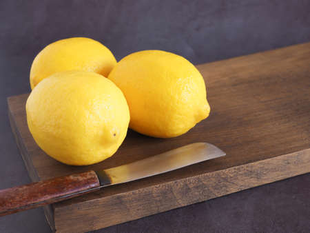 Lemons fruit on wooden cutting board with knife and have a dark grey background is a good source of Vitamin C, which helps control weight and Reduce Cancer risk. Copy space for text.の写真素材