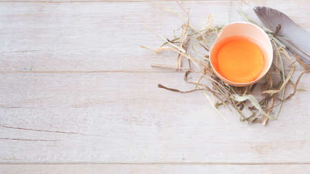 Organic egg half-cracked with yolk on straw over white wooden background. Concept food of healthy.