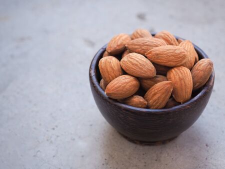 Organic almonds seeds in a wooden bowl put on a grey concrete background. Copy space for text.の写真素材