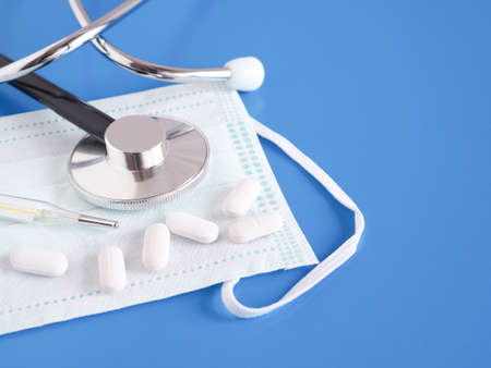 A pill, Thermometer, stethoscope and protective face mask on the blue background. Health concept. Copy space.の写真素材