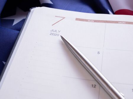 The pen point to July 2020 in a diary, put on American flag background.