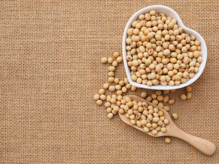 Soybeans in a heart-shaped bowl and wooden scoop on sackcloth background. Healthy food concept. Plant protein. Top view with copy space.の写真素材