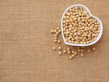 Soybeans in a heart-shaped bowl on sackcloth background. Healthy food concept. Plant protein. Top view with copy space.の写真素材