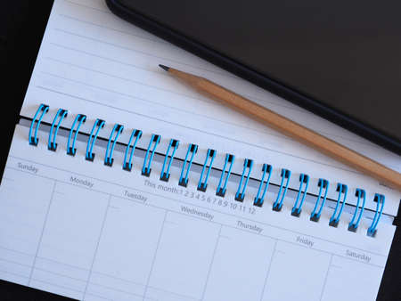 Weekly planner with pencil and smartphone on black background.