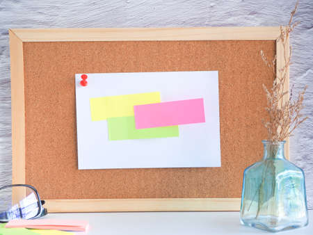 Colorful paper note pinned on a corkboard with glasses, pencil and dried caspia in the vase on white background.の写真素材