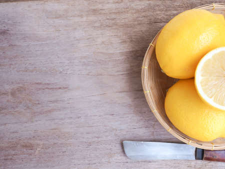 Lemon fruit and half in wicker basket with knife on wooden background, Copy space for text. Top view.の写真素材