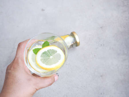 Hand holding glass of water and lemons slice with mint leaves over grey background. Copy space for text. High Vitamin C.の写真素材