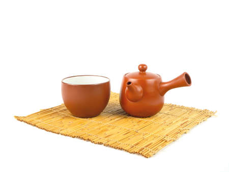 Brown clay teapot and cup on a bamboo mat isolated on a white background. Traditional Asian Tea set, space for text.の写真素材