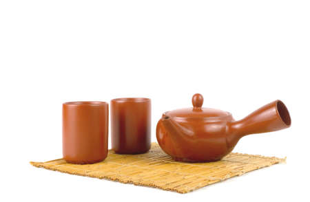Brown clay teapot and cup on a bamboo mat isolated on a white background. Traditional Asian Tea set, space for text.の写真素材
