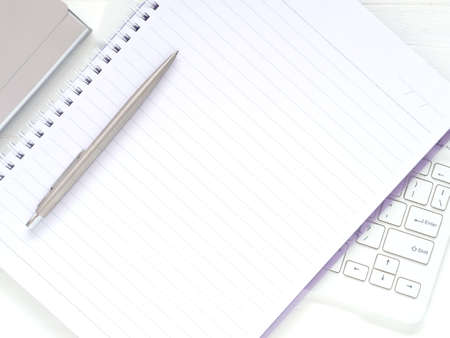 Flat lay white office desktop with blank notebook and pen put on the keyboard. Top view with space...