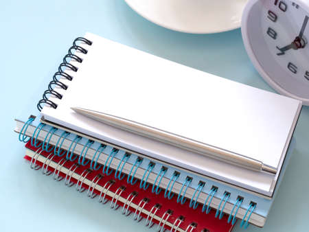 Stack blank notebook and pen with clock at 7:00 am on the blue workplace desk table. Business and...
