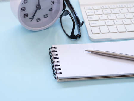 Blue workplace desk table with a notebook and pen, eyesglass, keyboard, clock at 7:00 am. Business and education concept. Space for text.の写真素材