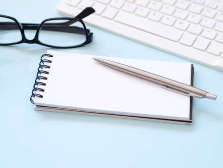 Blank notebook and pen on blue work place desk table, with eyesglass. Space for your text. Business...
