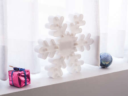 Snowflake and gift box, ball on the window sill with white curtains as background.の写真素材