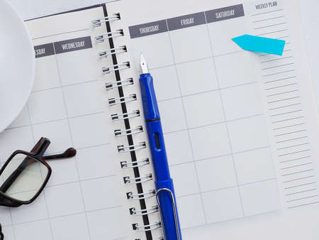 Pen on a page of a weekly plan with  note, glasses on the white office desktop. View from above, flat lay. Business and education concept.の写真素材