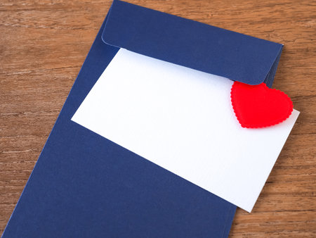 White card with red heart on blue envelope over wooden background. Close up with copy space.の写真素材