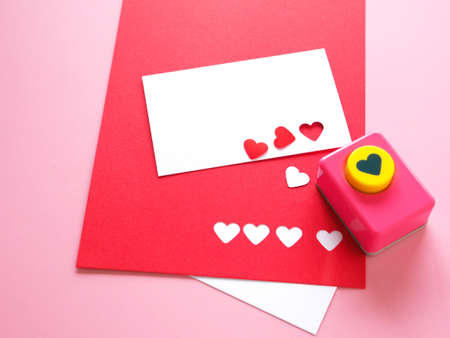White and red paper, heart-shaped punches and decorations for making a love card on a pink background. Space for your text.の写真素材