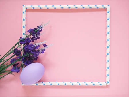 Easter egg and purple artificial flower bouquet in star-shaped paper tube frame on pink background, top view and copy space. Festive concepts.の写真素材