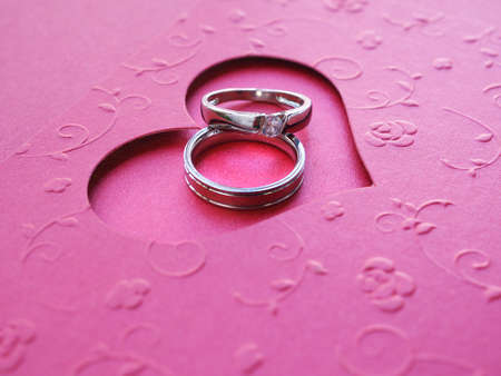 Close up two silver rings on a red heart-shaped card over red paper background with copy space. Concepts Valentine's Day, anniversary and wedding.の写真素材