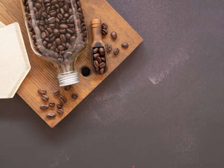 Top view, flat lay roasted coffee beans in glass bottle and wooden scoop, filter over rustic wood on drak grey background, space for your text.の写真素材