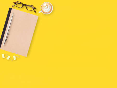 Flat lay yellow office desktop with notebook and pen, eyeglasses, coffee. Top view with space for...