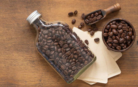 Top view, flat lay roasted coffee beans in glass bottle and wooden scoop, bowl, filter over rustic wood background, space for your text.の写真素材