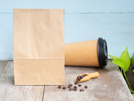 Roasted coffee beans in craft paper bag with wooden scoop, cup on wooden table. Mouckup, template with copy space for your text or logo.の写真素材