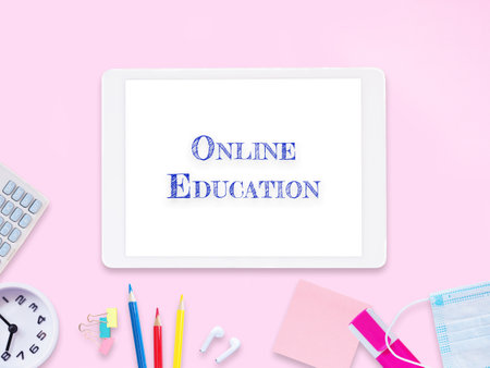 The word "Online Education" on tablet pc screen with stationery and white clock on pink workplace background. E-learning Concept.の写真素材