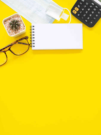 Blank notepad and eyesglass, hand sanitizer alcohol gel, medical face mask, cactus. on yellow work...
