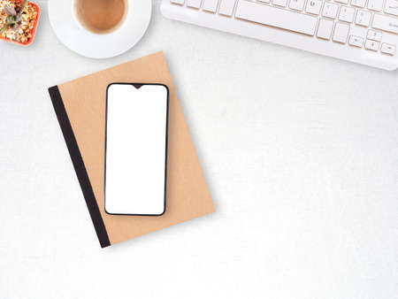 Smartphone on notebook and keyboard, coffee in white cup, cactus over the modern white desktop workplace. top view, flat lay with copy space. Business and education concept.の写真素材