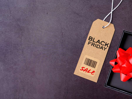 Top view, brown tag with text "Black Friday Sale" and black gift box with red bow on dark grey background. Flat lay, copy space.の写真素材