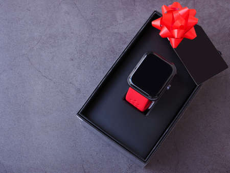 Smartwatch in the black gift box tied with a red bow and black greeting cards on dark grey background. Top view, flat lay with copy space. The concept for the season of giving.の写真素材