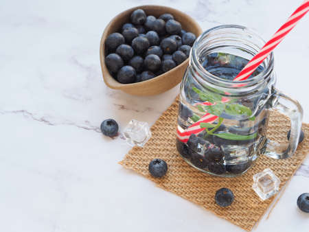 Infused water with fresh organic blueberries and drinking straw on marble background. Space for your...