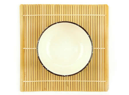Top view, empty beige ceramic bowl on bamboo mat isolated on a white background.  Use for home or restaurant, food design. Kitchen accessory. Japanese styleの写真素材
