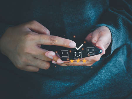 Customers using smartphone to send satisfaction surveys with smiley face icon of 3 stars. Customer service evaluation, Experiences, Feedback, and Satisfaction survey concept.の写真素材