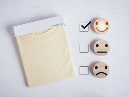 Review of yellow t-shirt for kids on white wooden table. smiley face icon showing customer satisfaction. Customer service evaluation, Experiences, Feedback, and Satisfaction survey concept.の写真素材
