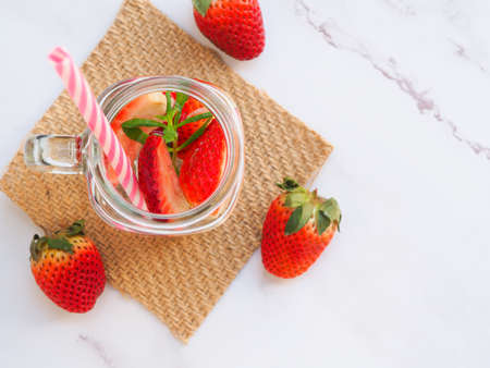 Infused water of strawberry in mason jar and straw on marble table. Healthy drink, Top view, space...