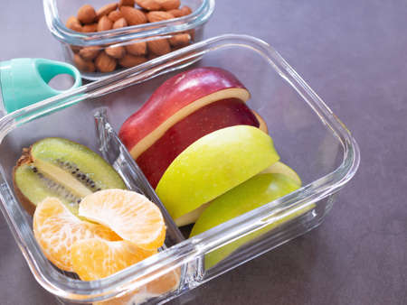 Glass container lunch box fresh fruit with apple, kiwi, orange and water bottle, almond on grey background. Take away food. copy space, healthy eating concepts.の写真素材