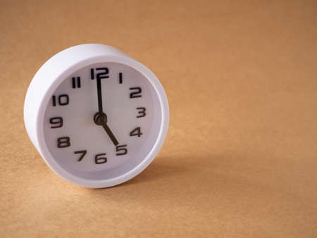Close up, white clock shows time at 5 o'clock on the office brown workplace tabletop. Copy space for your text. Business and education concept.の写真素材
