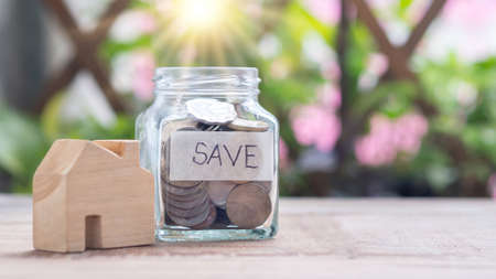 Close-up of a coin in bottle and a wooden house in sunlight with the word save label on wooden table...