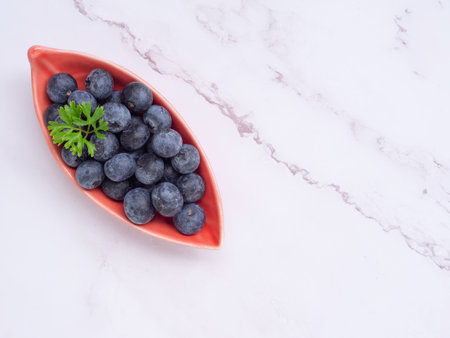 Top view, fresh blueberries in leaves-shaped red plate on grey background. Flat lay with copy space. Concept for healthy eating and nutrition, Superfood.の写真素材